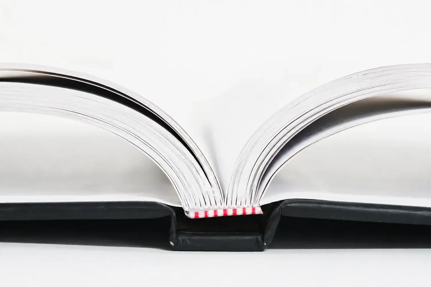 Close-up of Smyth-sewn hardcover binding construction for coffee table books, showing sewn signatures, endpapers, hinge score, and head/tail bands